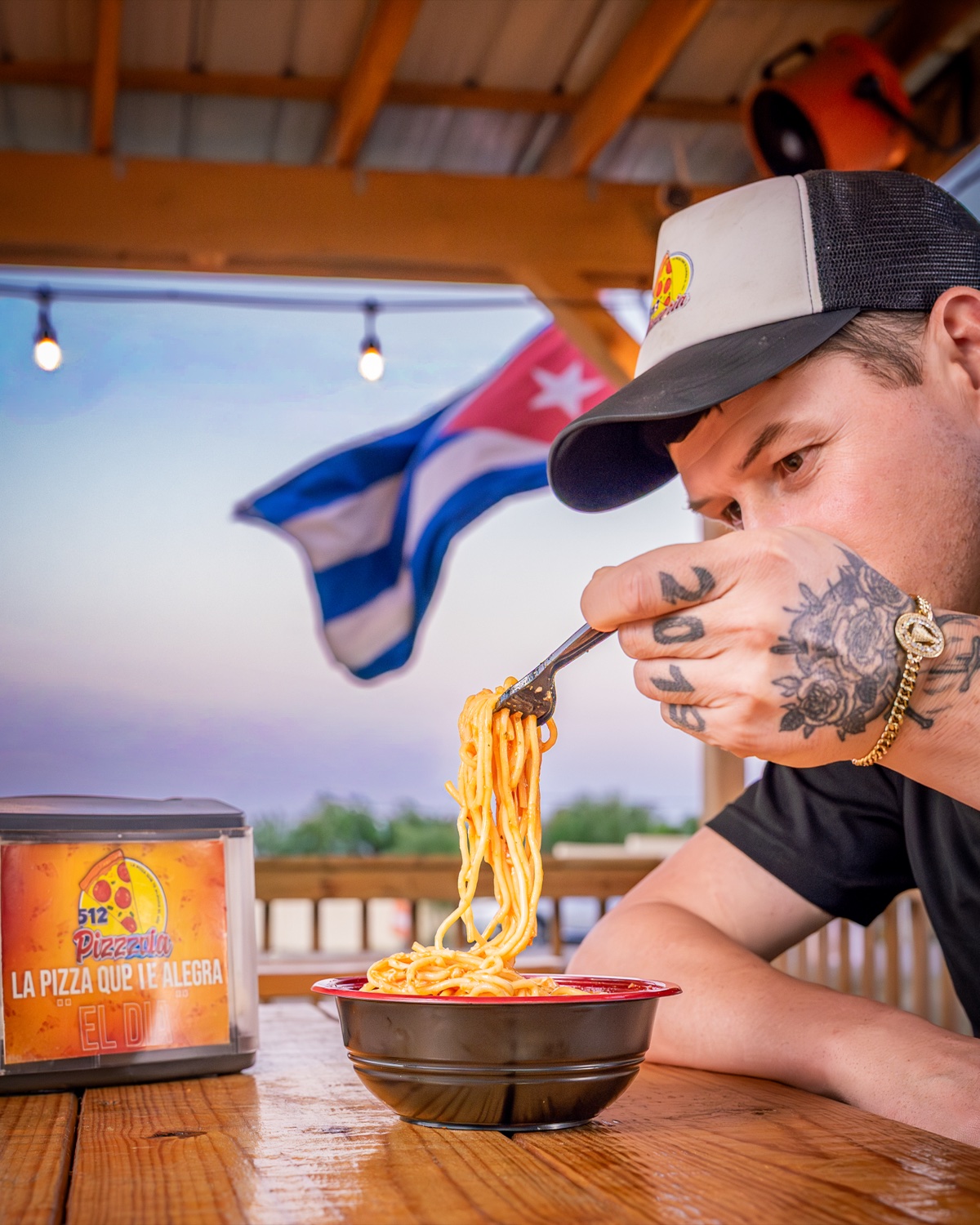 512 Pizzeria team member eating spaghetti at terrace with Cuban flag — Pflugerville