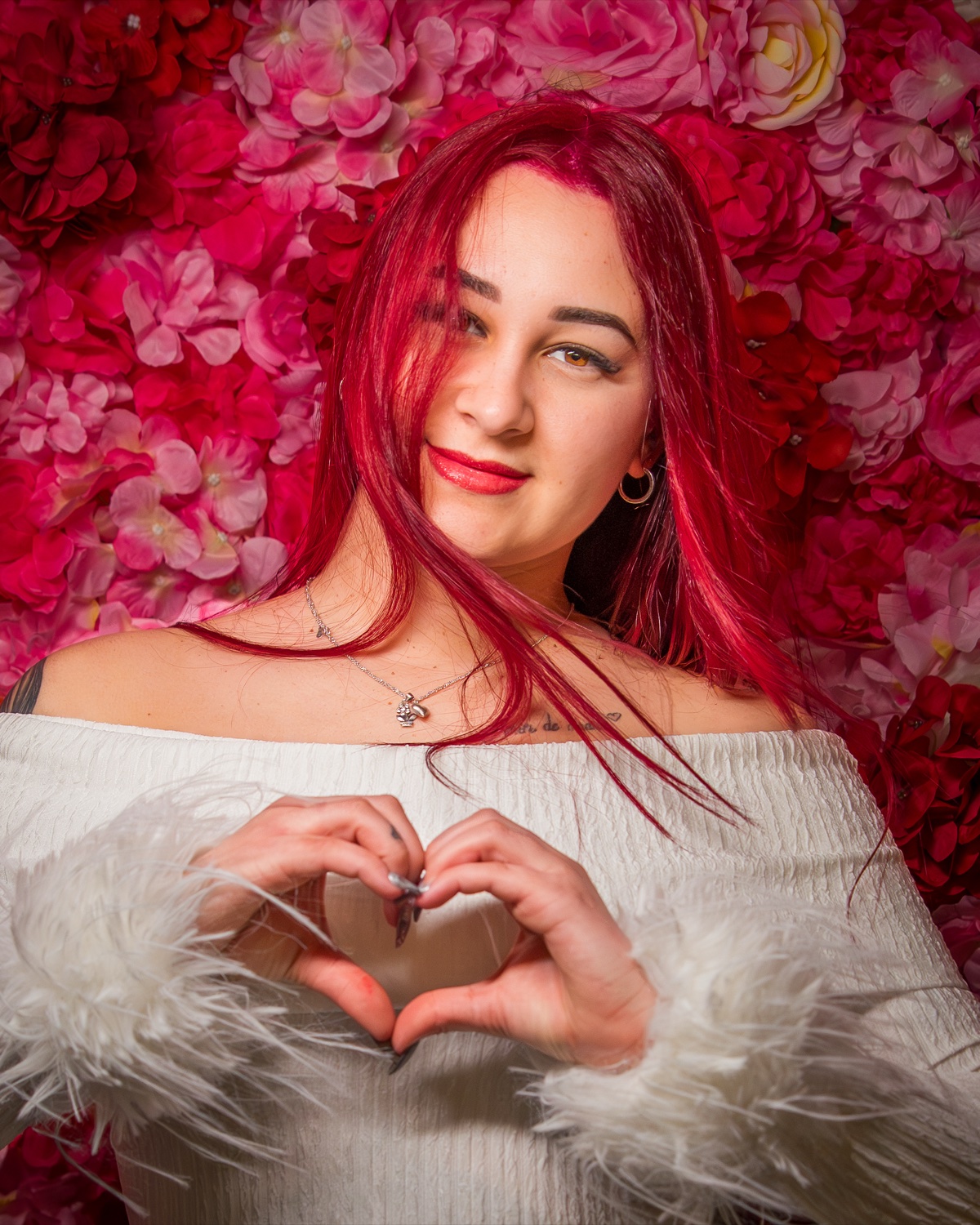 Editorial Valentine portrait, red hair, rose-wall backdrop, heart hand gesture — Austin photographer
