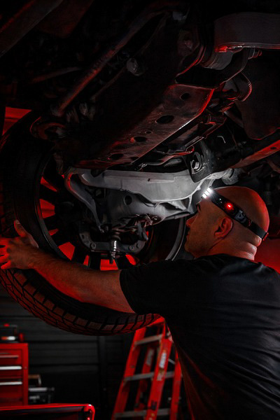 Mechanic under car with red shop lighting — branding photography for The Mechanic ATX